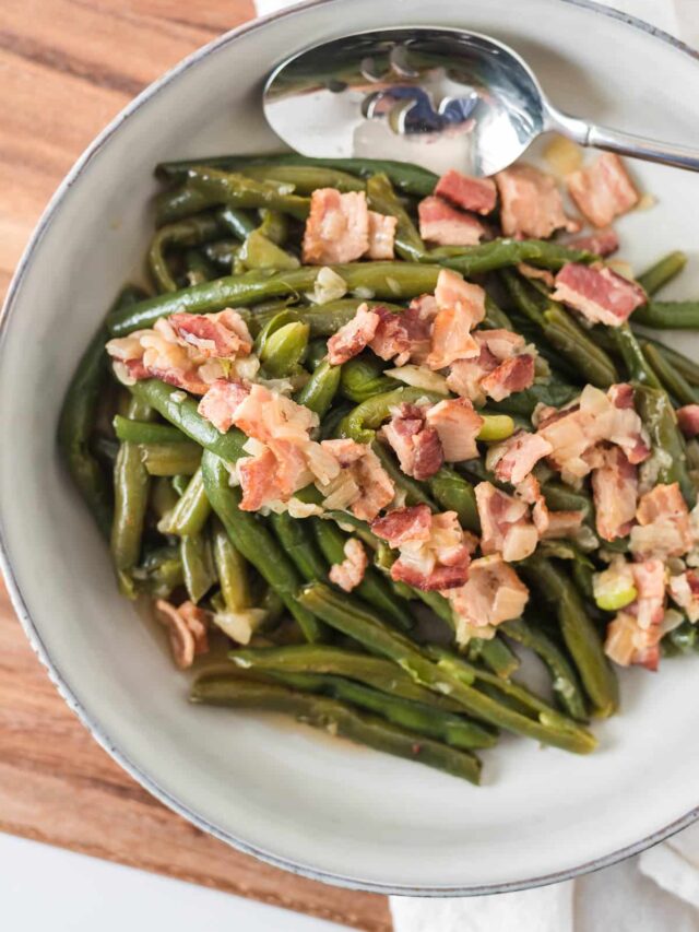 overhead closeup of german green beans with bacon in serving dish with spoon