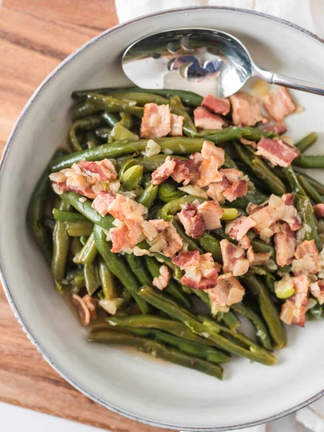 overhead closeup of german green beans with bacon in serving dish with spoon