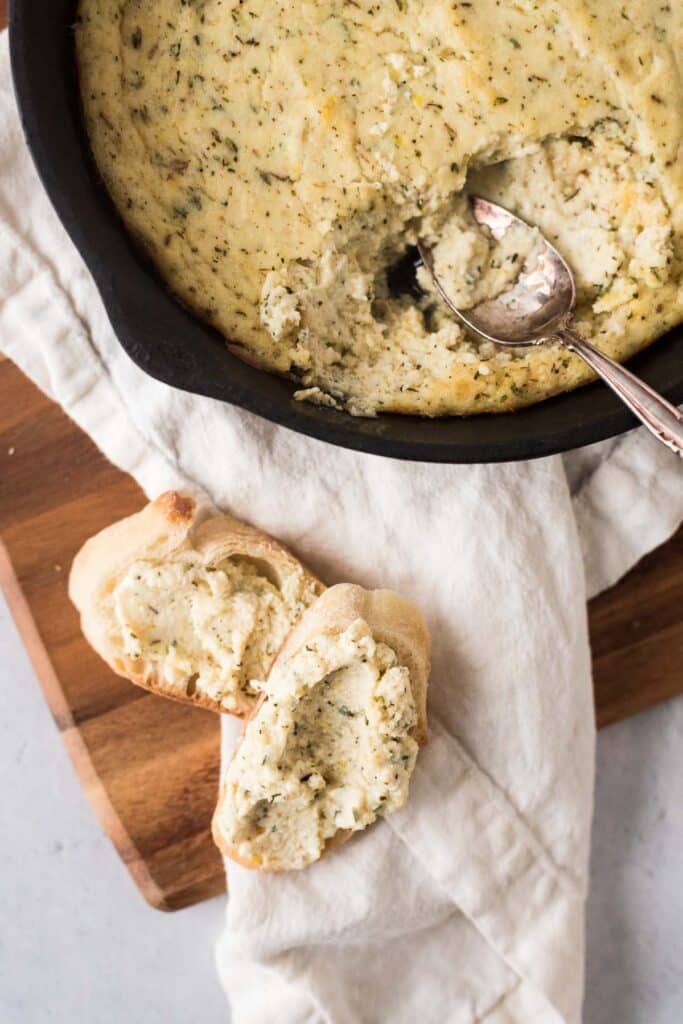 Baked rirotta in cast iron skillet with spoon and two slices of bread with cheese dip on them