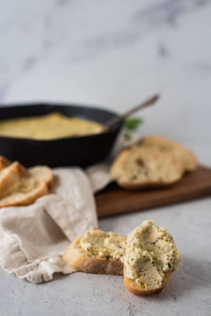 baked ricotta on slices of baguette with cast iron skillet in background