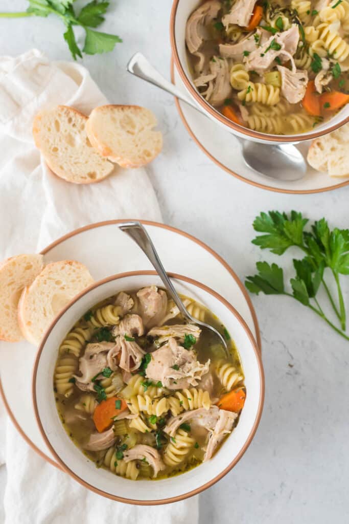 bowl of turkey noodle soup on plate with pieces of baguette