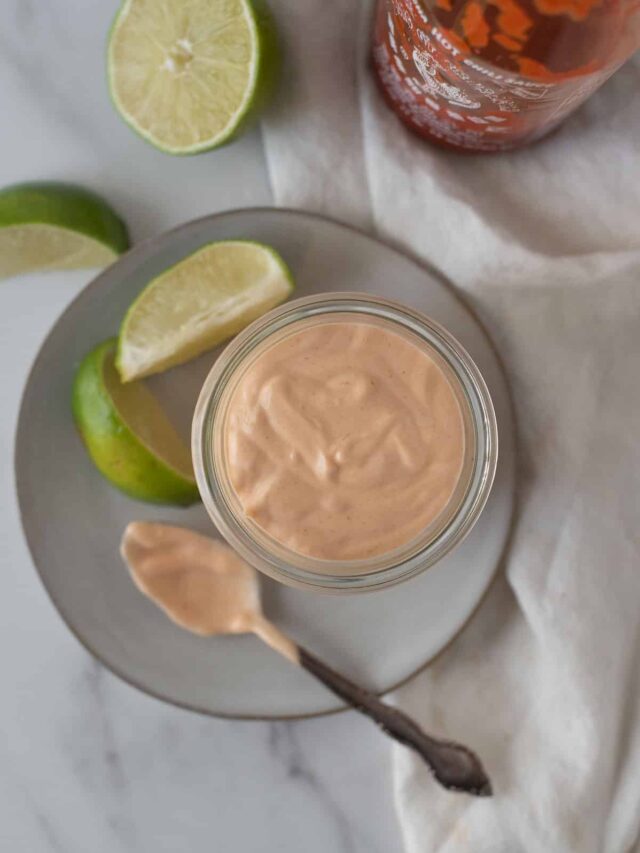 overhead view of spicy mayo in bowl with spoon beside bowl and lime wedges behind