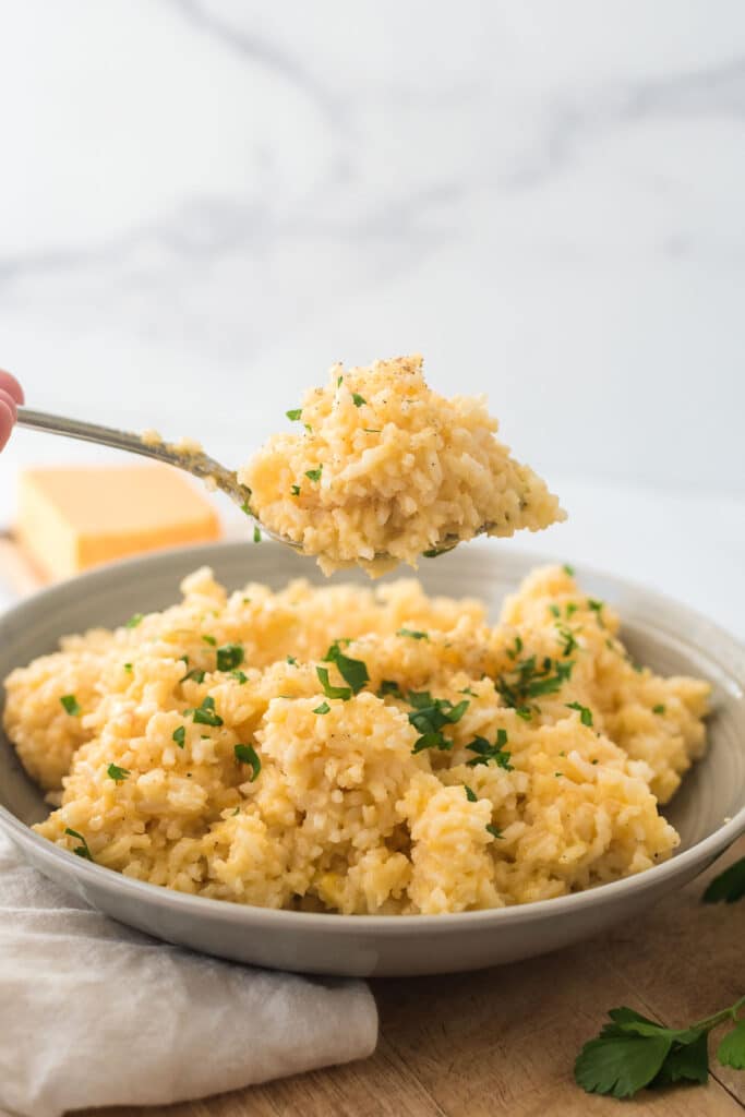 spoon lifting portion of cheesy rice out of grey bowl