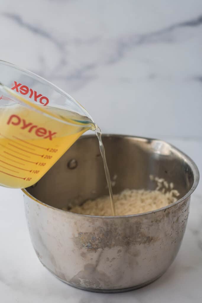 chicken broth being poured into saucepan with rice