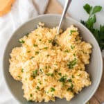 cheesy rice in grey bowl with serving spoon