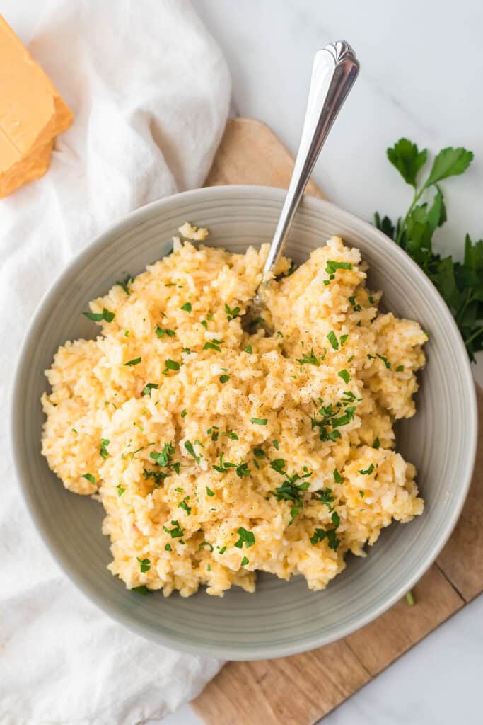 cheesy rice in grey bowl with serving spoon