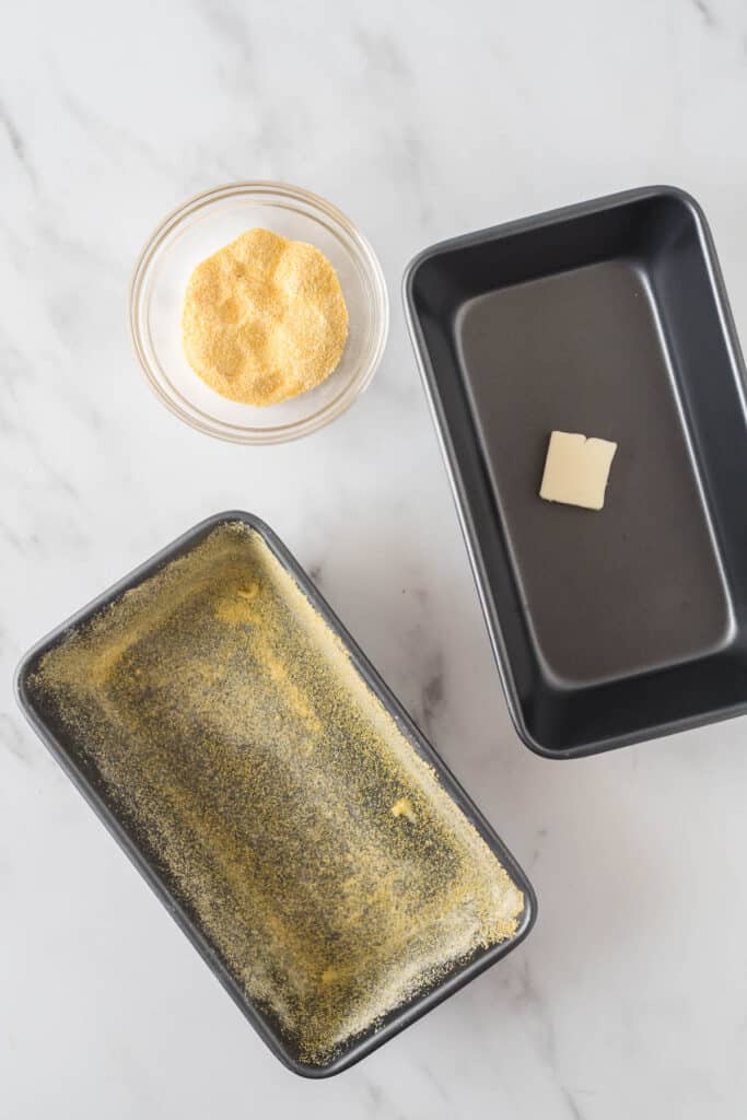 two loaf pans, one with butter and one with butter and cornmeal next to small bowl of cornmeal