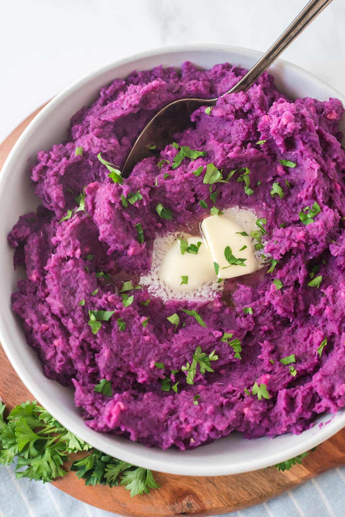 white bowl filled with mashed purple sweet potatoes topped with a pad of butter and fresh parsley