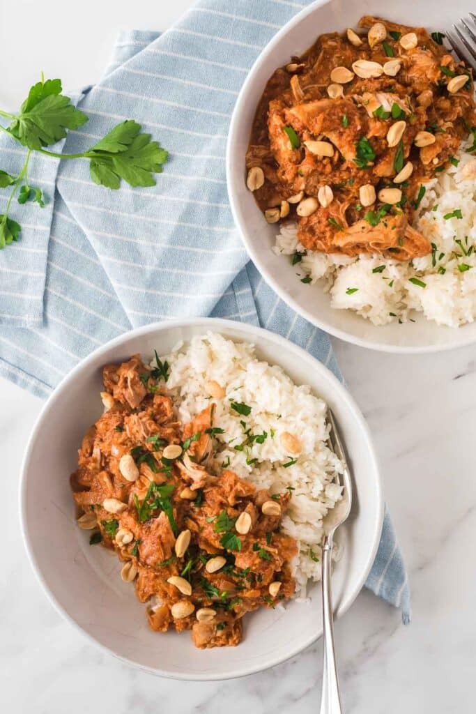 two bowls of peanut stew with chicken and rice topped with parsley