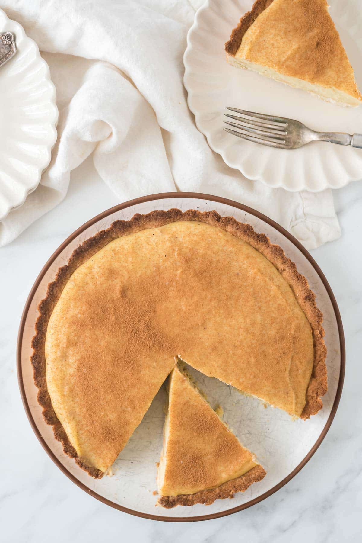 Milk tart on serving platter with cut piece at an angle and two plates with other slices in background
