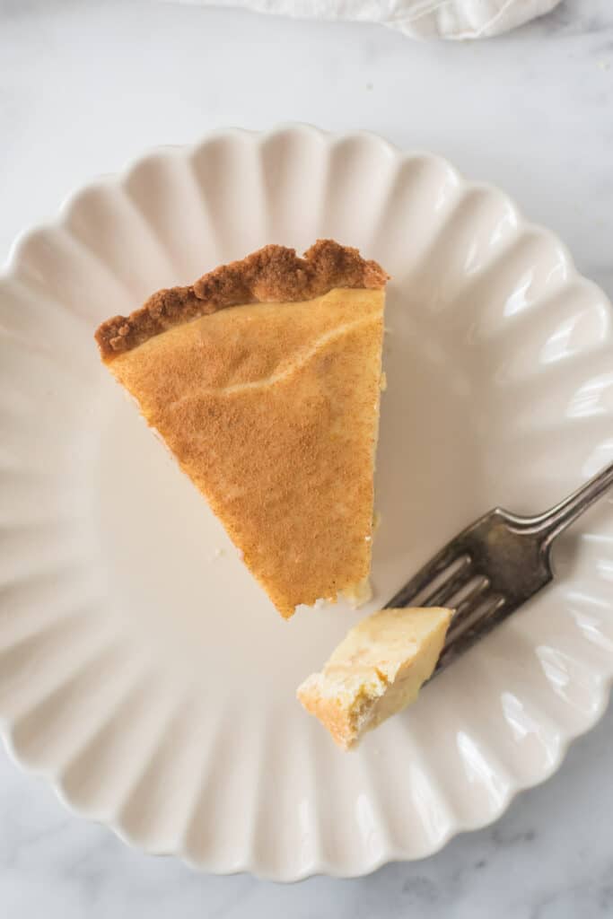 slice of milk tart on white plate, fork on plate with a bite of tart on it