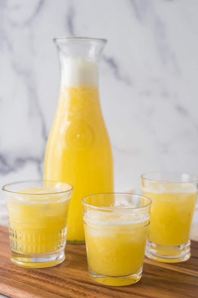 three glasses of pineapple ginger juice with glass pitcher in background