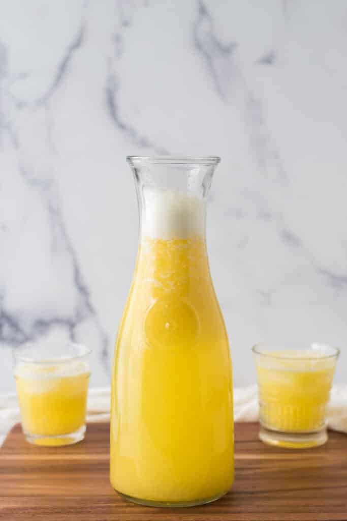 pitcher of pineapple ginger juice in front with two glasses of juice in background on either side