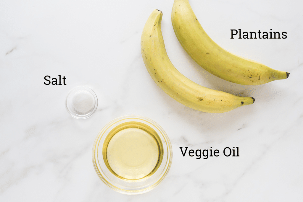 plantains, bowl of veggie oil and small bowl of salt on marble with text labels