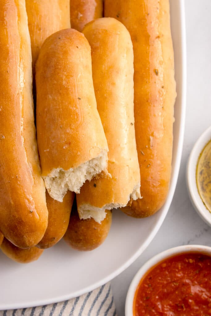 White platter of breadsticks with top breadstick torn in half