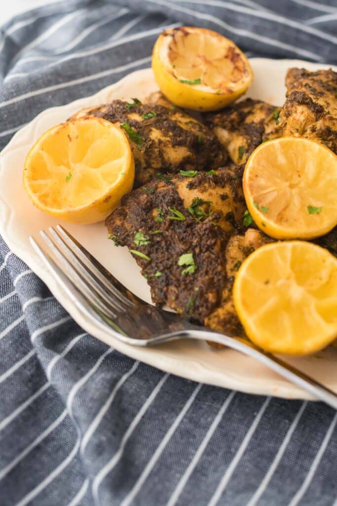 close up of white platter with roasted chicken thighs and halved lemons and serving fork