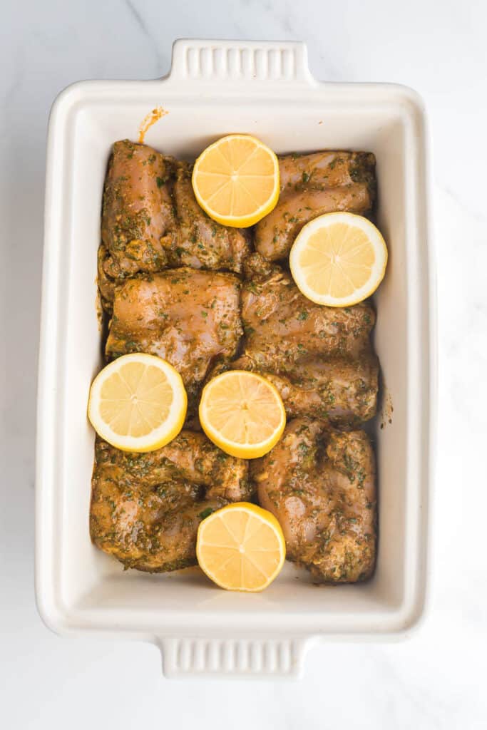 chicken thighs with chermoula sauce in baking dish with halved lemons ready to bake