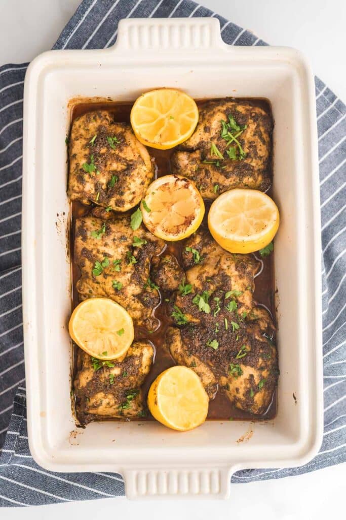 overhead view of baking dish with baked chicken thighs in chermoula sauce with lemons
