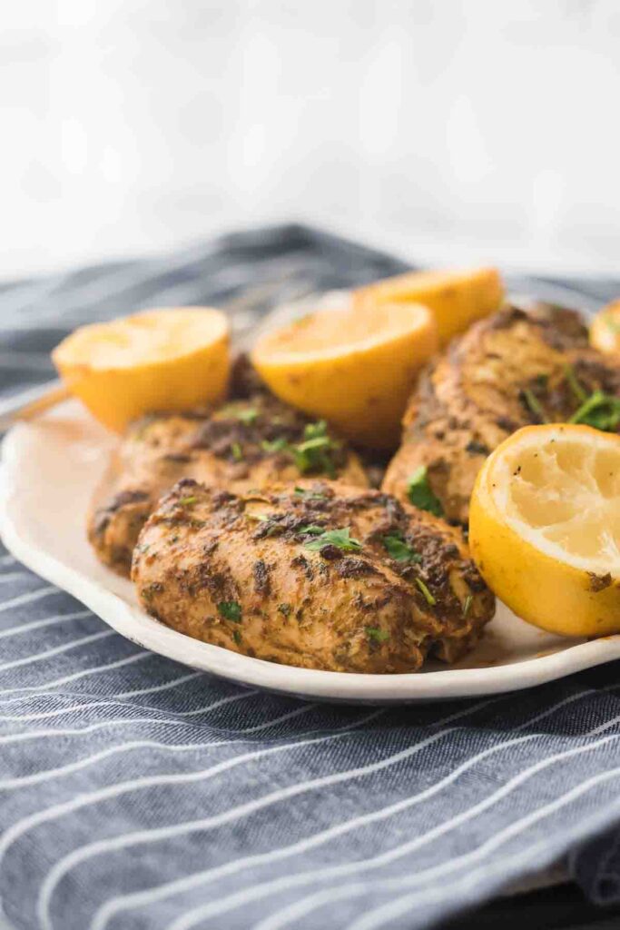closeup of chicken thighs on white platter with halved lemons