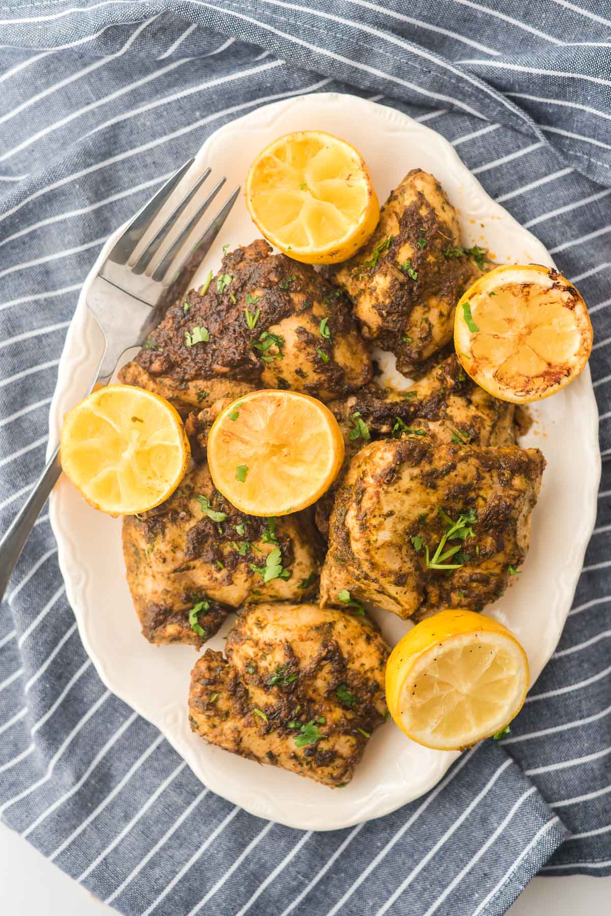 white platter with roasted chicken thighs in red chermoula sauce with sliced lemons