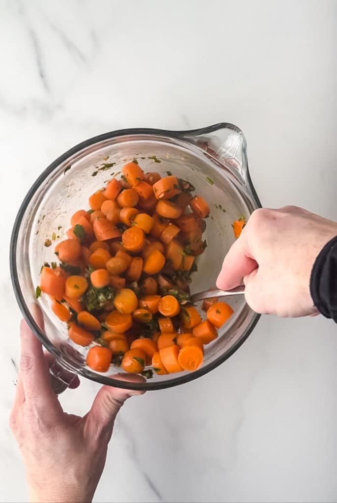 tossing cooked carrot slices with herb dressing