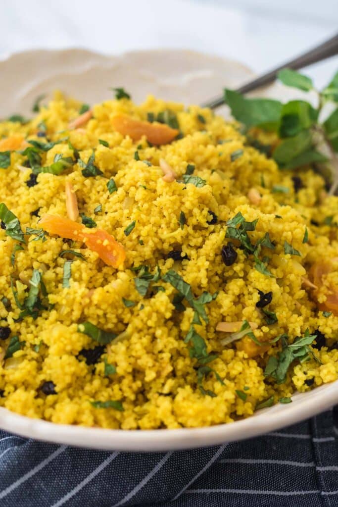 closeup image of couscous in white bowl with fresh mint garnish