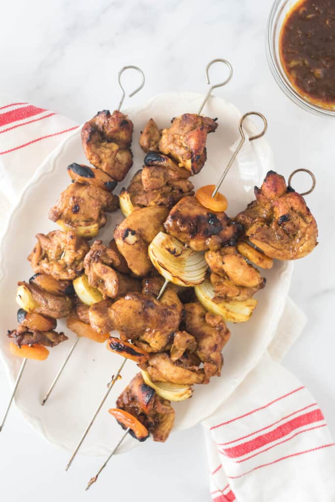 chicken skewers with onions and apricots stacks on white platter