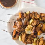 grilled skewers of chicken, onion and dried apricots on white platter with small glass bowl of glaze beside