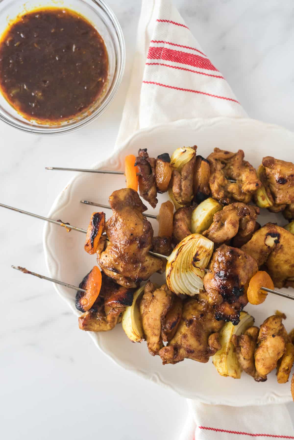 grilled skewers of chicken, onion and dried apricots on white platter with small glass bowl of glaze beside