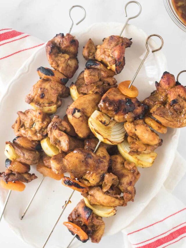 chicken skewers with onions and apricots stacks on white platter