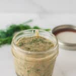 small mason jar filled with mustard and dill sauces with jar lid and fresh dill in background