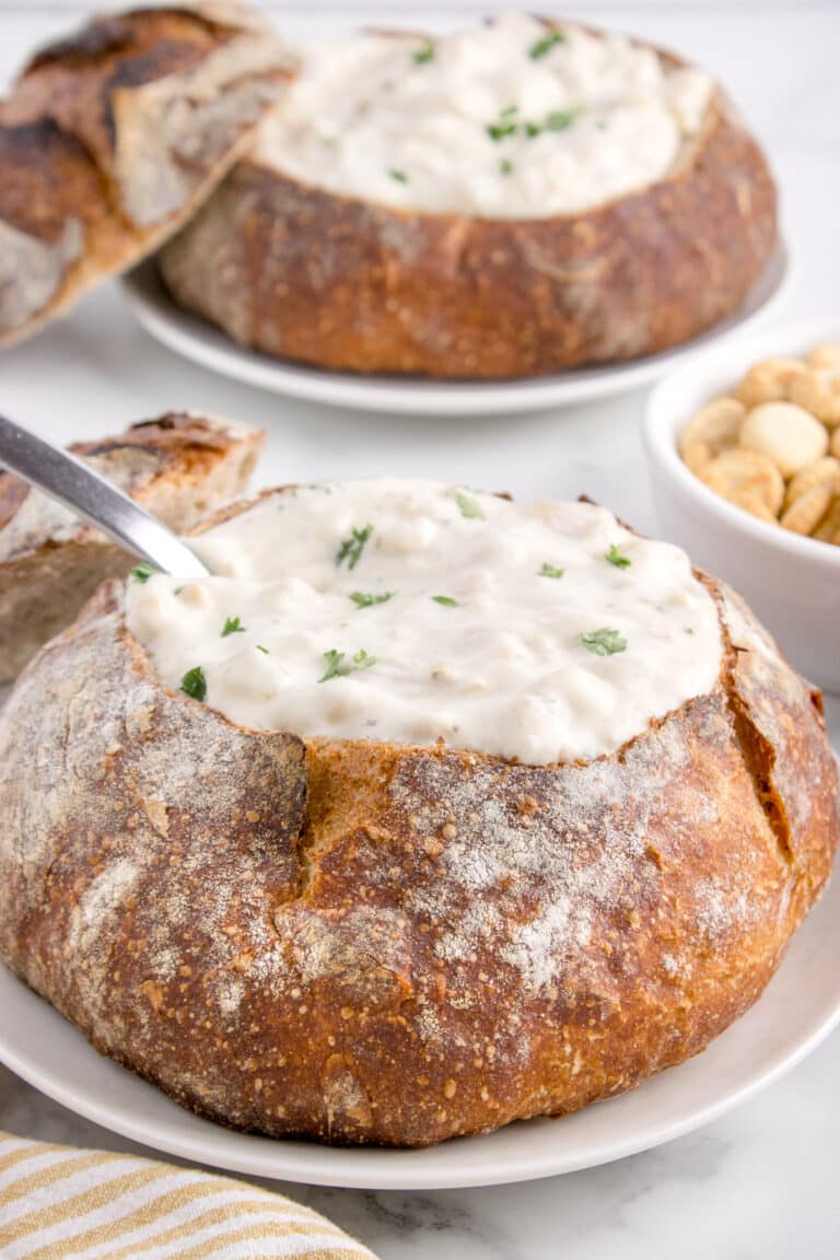 two sourdough bread bowls on plates filled with chowder and spoons
