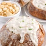 two sourdough bread bowls on plates, filled with chowder and soup crackers behind