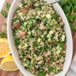 overhead view of tabbouleh in white serving bowl with spoon, cut lemon and fresh parsley tucked around bowl
