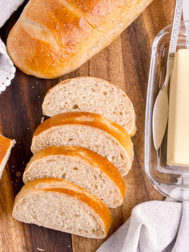 sourdough french bread slices stacked next to second loaf and stick of butter