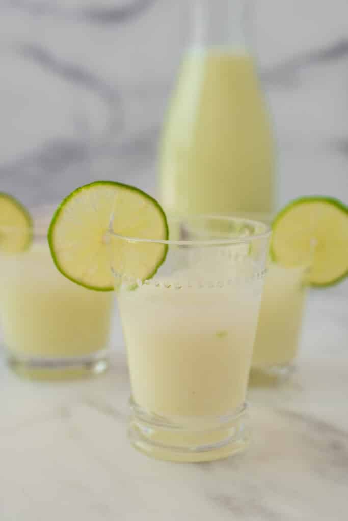 Brazilian Limeade in three glasses with lime wheel garnishes and pitcher in background
