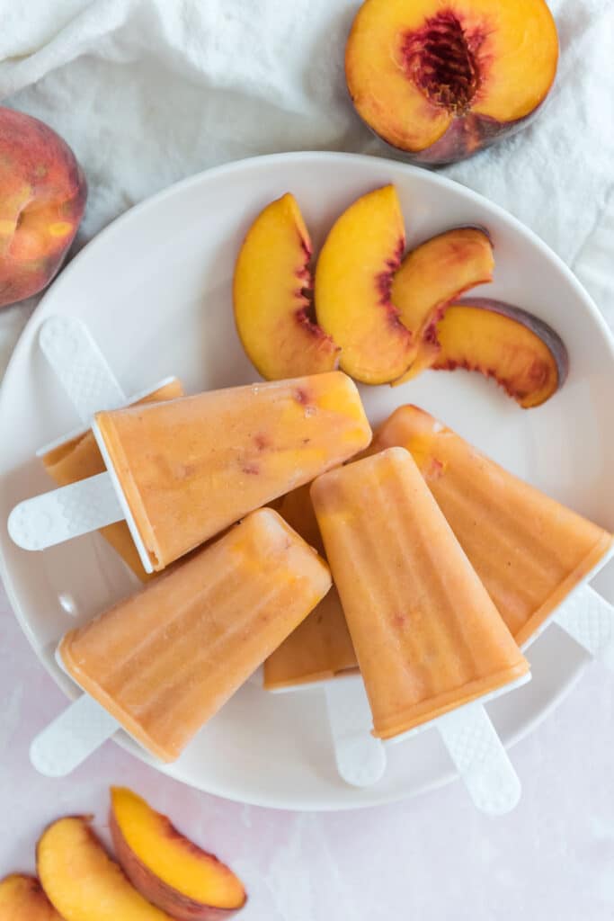 peach paletas on white plate with sliced peaches