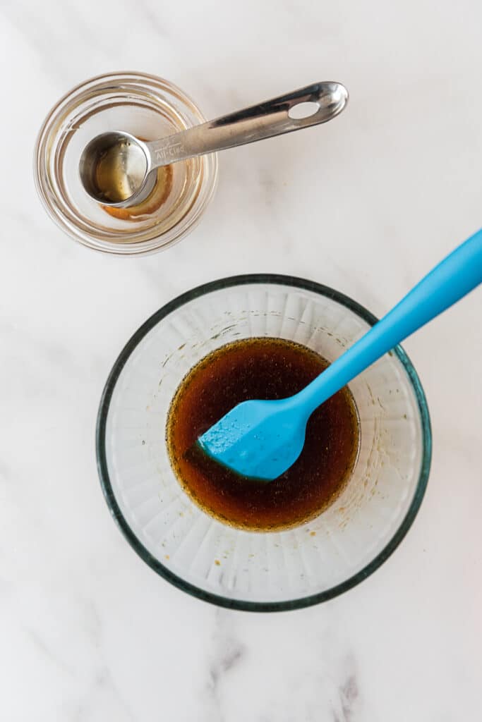 glass mixing bowl with dipping sauce being mixed by blue silicone spatula with empty smell bowls beside