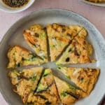 korean pancake cut into wedges on grey plate with bowl of dipping sauce on side