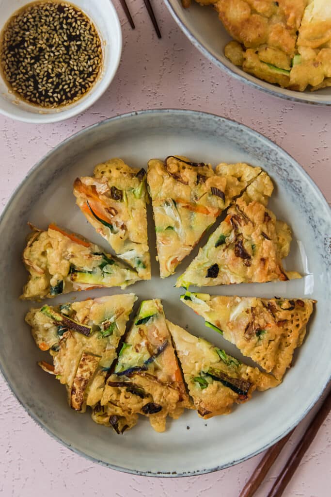 korean pancake cut into wedges on grey plate with bowl of dipping sauce on side