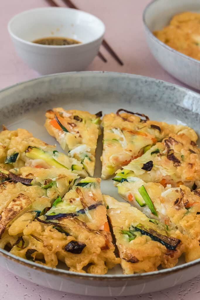 up close image of korean pancake cut into wedges on grey plate showing veggies 