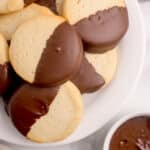 sourdough shortbread cookies piled on platter, with half of each cookie dipped in melted chocolate