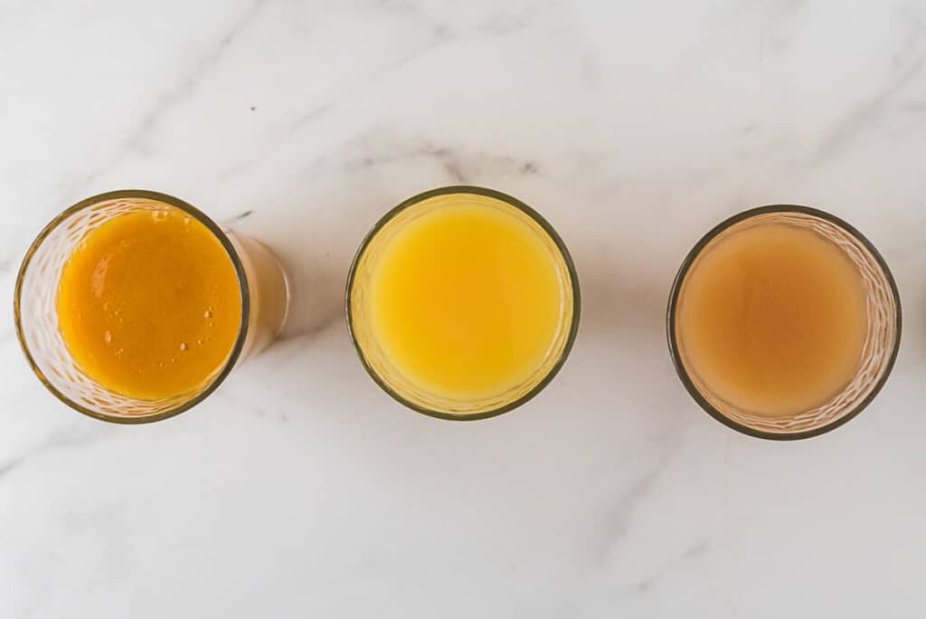 overhead view of three glasses with passion fruit juice, orange juice, and guava juice 