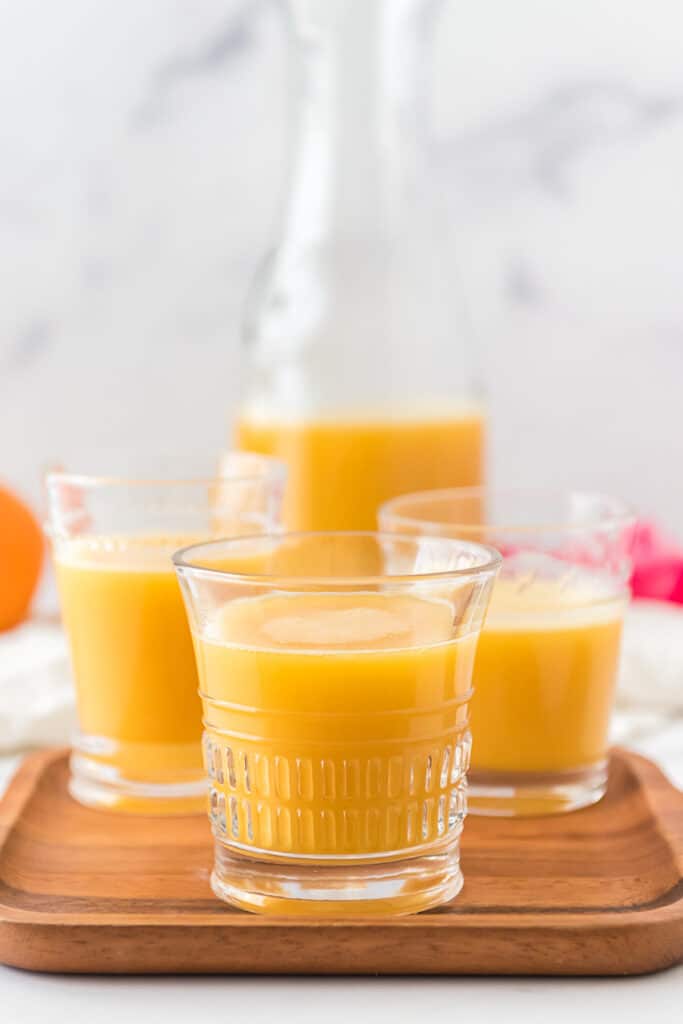 three small glasses with pog juice on wooden serving tray with pitcher in background