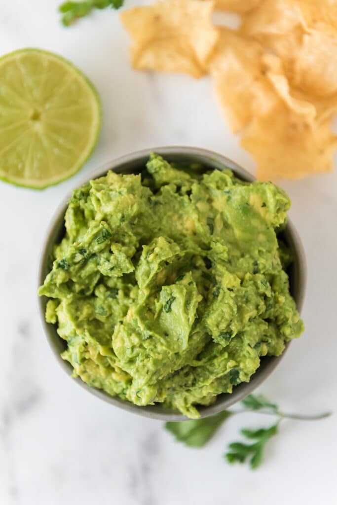 overhead view of guacamole in grey bowl with lime and chips around bowl