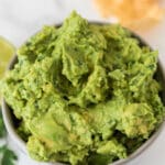 homemade guacamole in small grey bowl with chips blurred in background