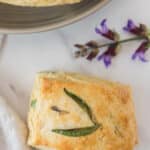 overhead view of lemon sage biscuit with sage leaves decorating the top of the biscuit and sage flowers beside it