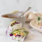 spring roll cut in half and stacked on top of each other, with plate and bowl of peanut sauce in background