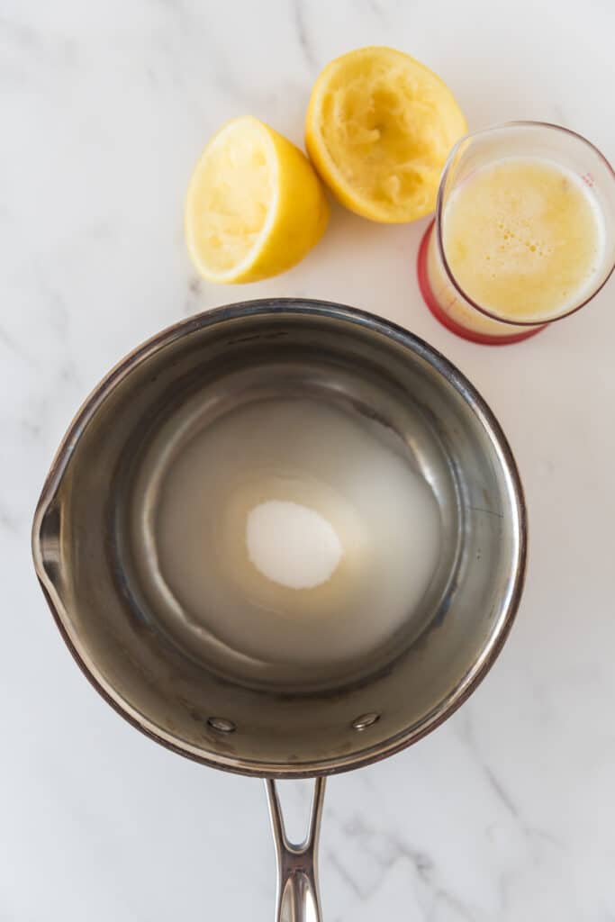 saucepan with sugar and water next to lemon juice and squeezed lemons