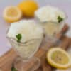two glass bowls with stems filled with lemon granita and garnished with small sprigs of mint, with lemon slices around